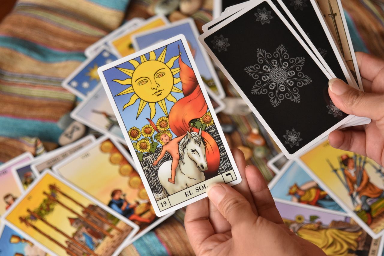 Close-up of tarot cards in hands, showcasing El Sol card. Ideal for fortune-telling and spirituality themes.