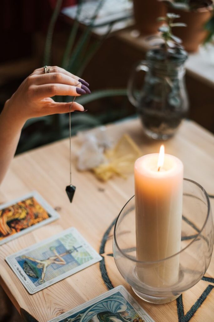 pexels photo 4790557 4790557 From above of crop anonymous female fortune teller with amulet on thread above tarot cards near burning candle on table